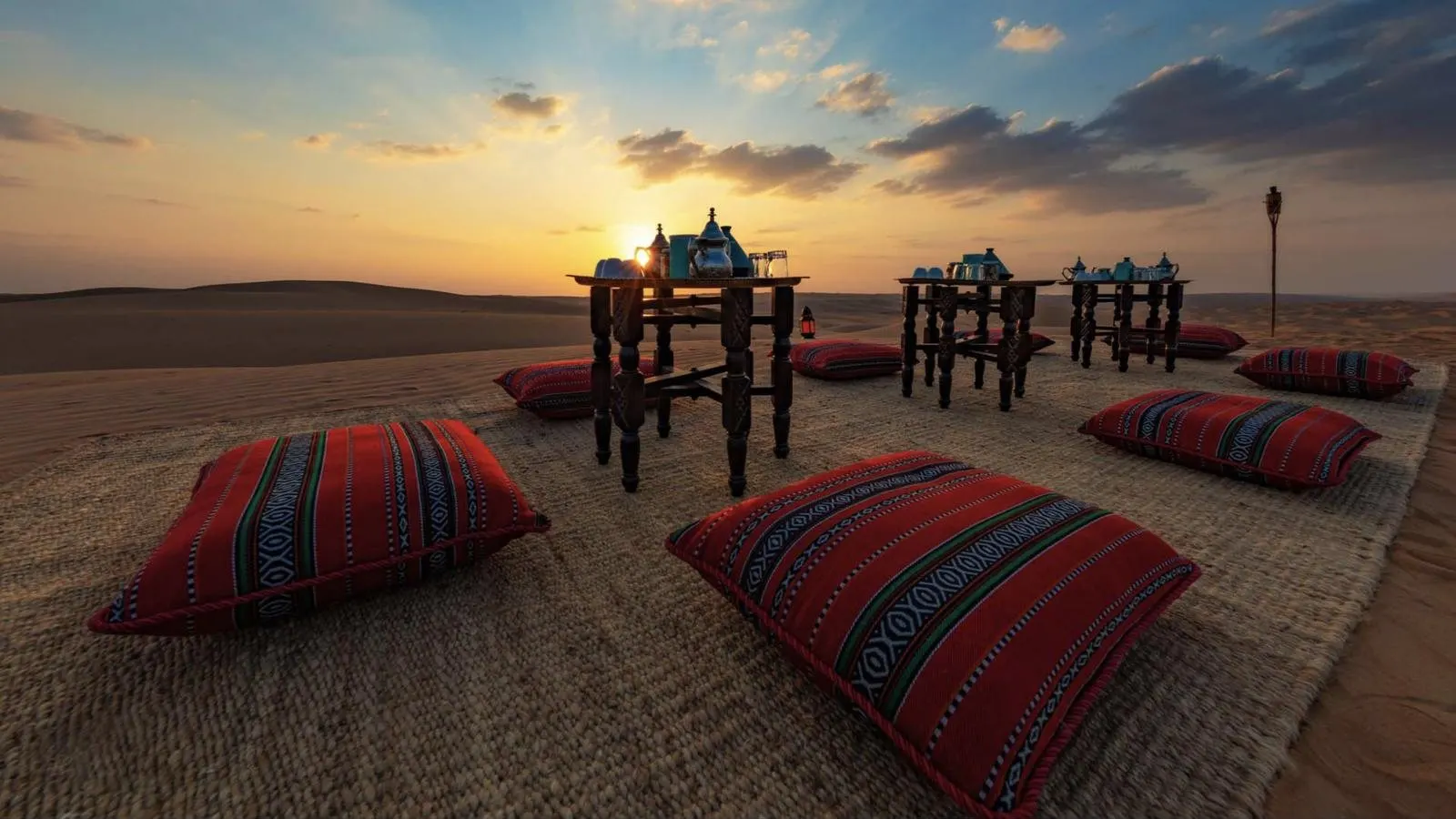 Tea tables and cushions laid out on the dunes at sunset